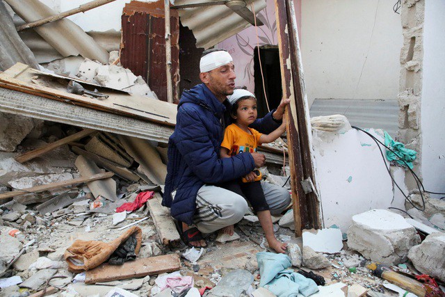 Hai cha con người Palestine bị thương ngồi trước một ngôi nhà trúng không kích của Israel ở Rafah, miền Nam Dải Gaza, hôm 1-5 Ảnh: REUTERS