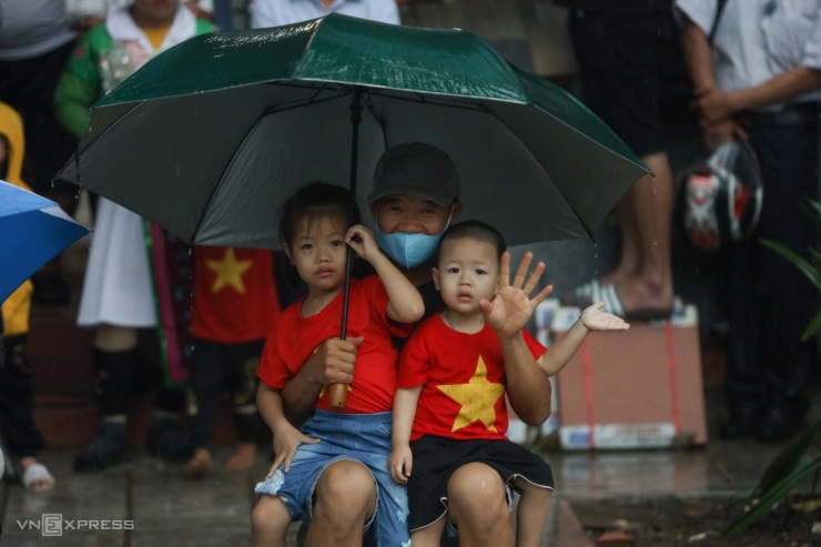 Ba ông cháu mặc áo mang hình cờ Tổ quốc đội mưa chờ xem diễu binh.