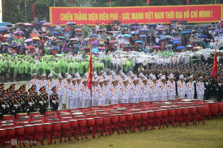 Trên sân vận động tỉnh Điện Biên, các khối quân đội, công an đứng nghiêm trang theo đội hình dưới trời mưa. Phía sau, người dân mang ô, áo mưa cũng đứng nghiêm trang, hướng về lễ đài để làm lễ chào cờ và nghe diễn văn khai mạc.