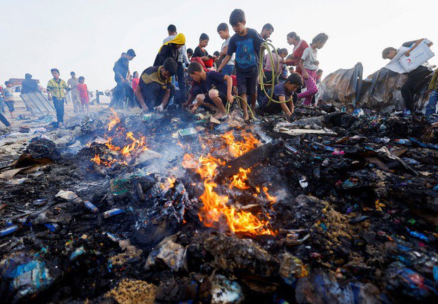 Người dân Palestine tìm kiếm thực phẩm từ đống tro tàn tại khu lều trại tạm cư ở Rafah sau vụ không kích đêm 27-5 của Israel. Ảnh: REUTERS