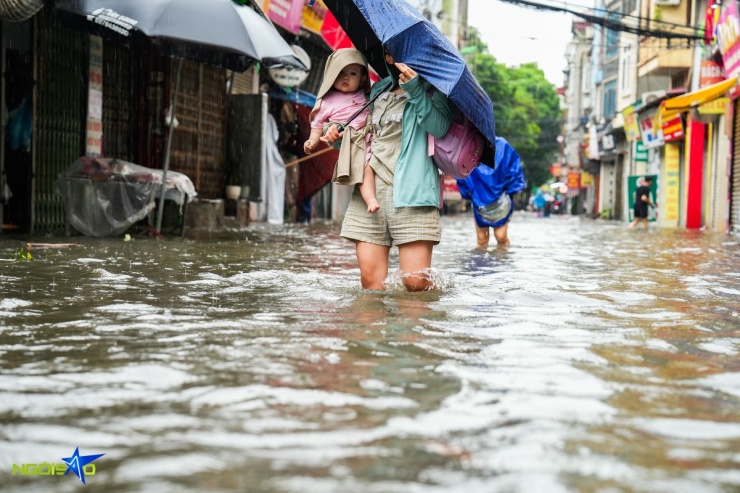 Người phụ nữ bế con đang bì bõm lội nước về nhà.