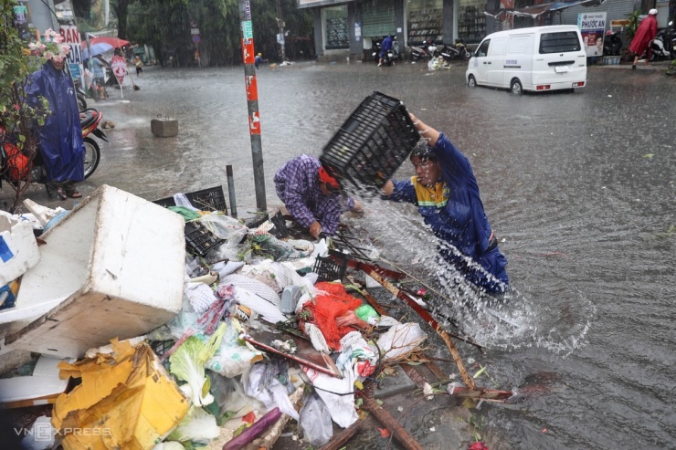 Tại cống thoát nước trên đường Lã Xuân Oai, các công nhân môi trường đội mưa để vớt rác thông cống. "Bao năm nay đoạn đường này có 300 m trũng thấp nên cứ mưa là ngập sâu", anh Tuyến nói, trong lúc khơi thông cống.