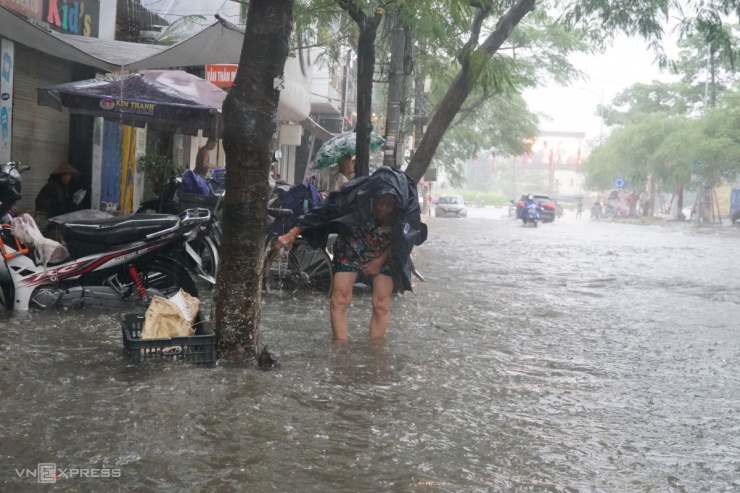 Cụ bà bán nước ở vỉa hè đường Lê Lợi, quận Ngô Quyền dùng tay móc rác khỏi miệng cống để nước thoát nhanh hơn. Đoạn đường qua cổng Bệnh viện Đa khoa quận Ngô Quyền ngập  khoảng 60 cm.