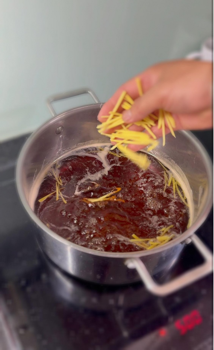 Cho phần nước đường vào nồi cùng 500ml nước lọc, đun sôi, đảo đều tay cho đường tan hết, rồi bỏ thêm cả gừng thái sợi