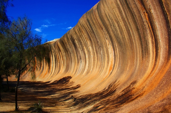 Dãy núi đá Wave Rock cách thành phố Perth bang Tây Úc khoảng 340km trông như cột sóng thần khổng lồ giữa sa mạc. Những làn sóng hình thành do đá bị nước mưa xói mòn từ hàng triệu năm và tùy vào thời điểm trong ngày, đá có màu đỏ, xám, cam, vàng.