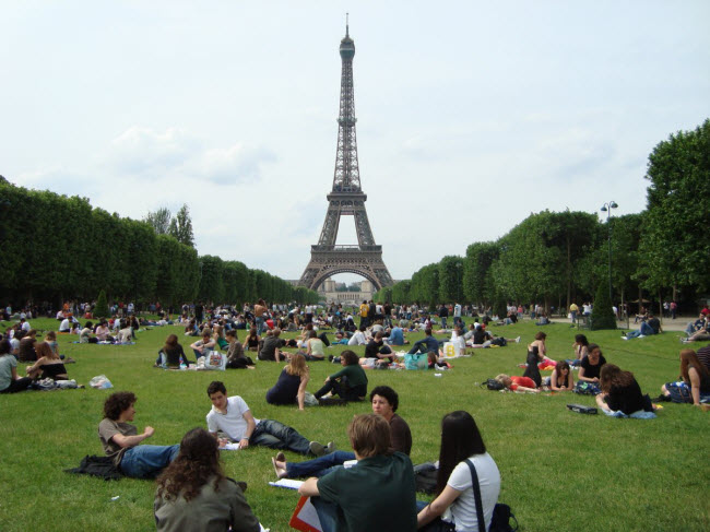 Du khách ngồi thư giãn trên bãi cỏ gần tháp Eiffel ở Paris, Pháp.