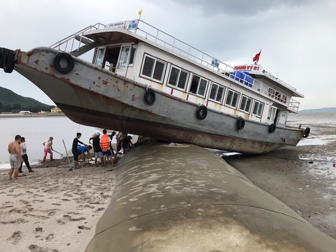 Chủ tàu phải thuê máy xúc, huy động người dân hỗ trợ để kéo tàu ra biển trước khi thủy triều dâng cao. Trong ảnh: Tàu Hoàng Vi 1 nằm "vắt vẻo" trên đê sau cú lao trực diện.