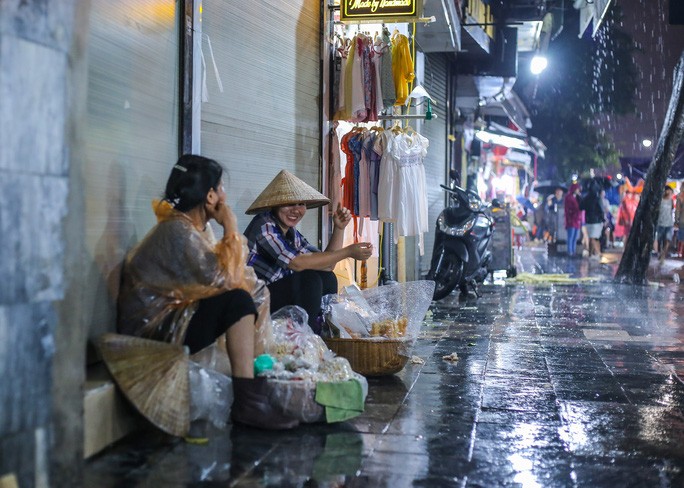 Cơn mưa nặng hạt, hai người phụ nữ bán hàng rong đang ngồi nghỉ ngơi dưới mái hiên