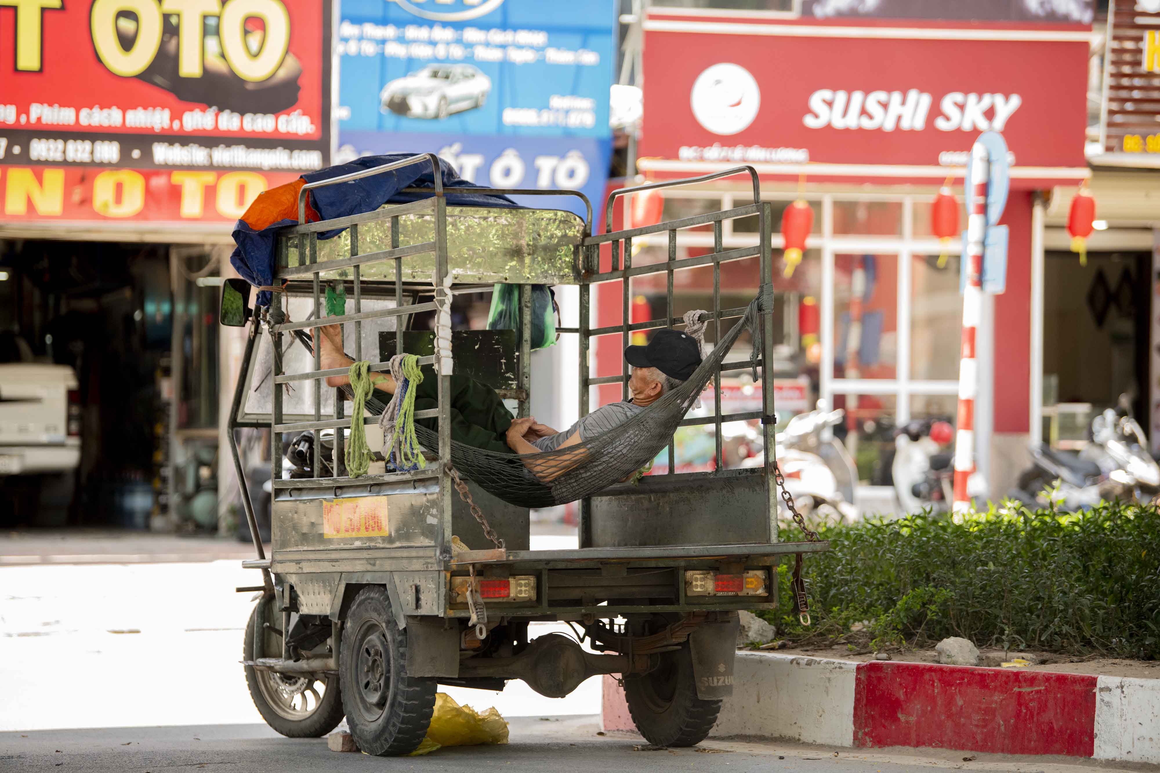 Chủ sở hữu những chiếc xe 3 bánh tận dụng thùng xe để mắc võng ngủ tránh cái nắng nóng gay gắt tại gầm cầu đường Lê Văn Lương. Một lao động cho biết: “Nắng nóng quá, buổi trưa tôi tranh thủ mang chiếu ra gầm cầu ngủ cho mát chứ ở chỗ trọ mái tôn hấp hơi xuống nóng như lửa đốt”.