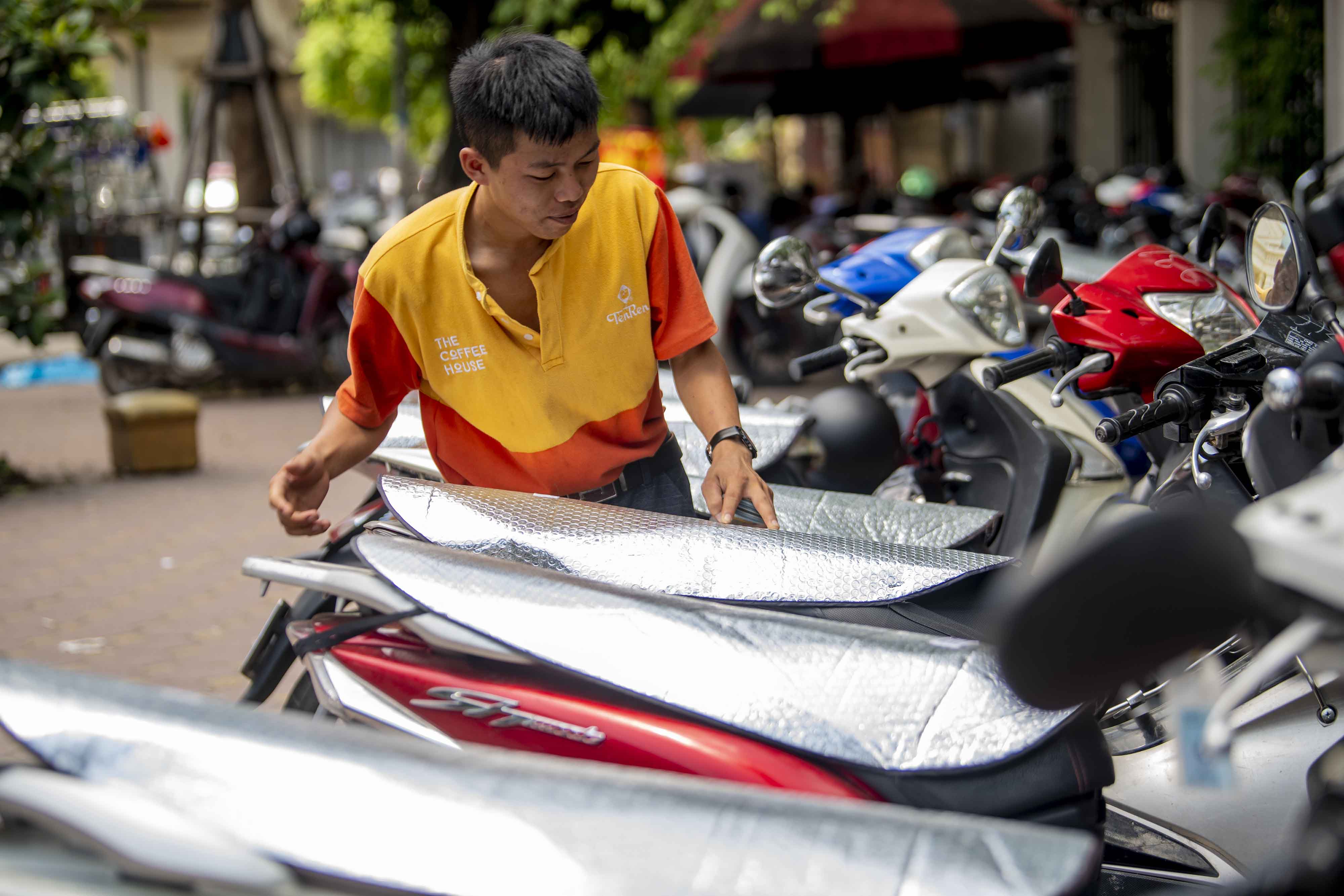 Một bảo vệ quán nước dùng các tấm chống nóng để che yên xe cho khách tránh nắng nóng.