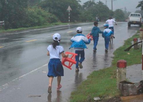 Các em cầm ghế nhựa và mưa ướt hết quần áo.