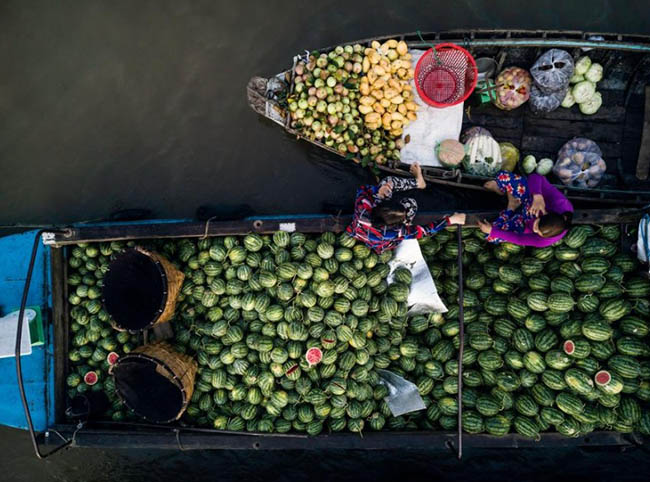 11. 2 người bán trái cây trò chuyện trong khi chờ đợi khách hàng tại chợ nổi Phong Điền ở đồng bằng sông Cửu Long. Ảnh: Carlos Antunes.
