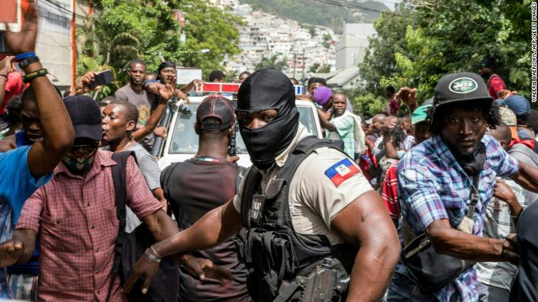 Người dân Haiti vây quanh xe cảnh sát chở các nghi phạm.