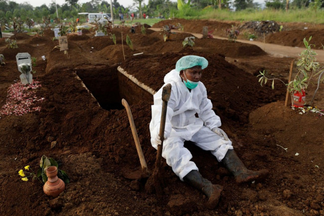 Người đào huyệt ở Indonesia mặc thiết bị bảo vệ cá nhân đang nghỉ ngơi sau khi chôn cất người tử vong vì COVID-19 ở Indonesia. Ảnh: Reuters.