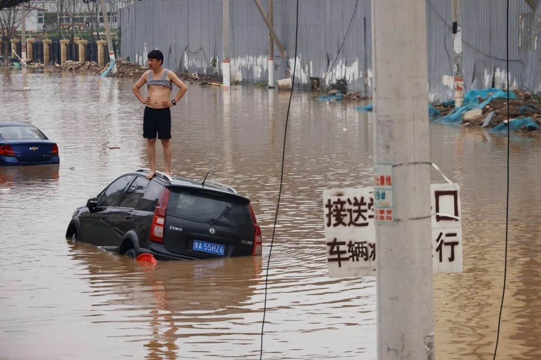 Một người đàn ông đứng trên ô tô bị nước lũ vây quanh ở thành phố Trịnh Châu, tỉnh Hà Nam, Trung Quốc hôm 22/7. Ảnh: Reuters