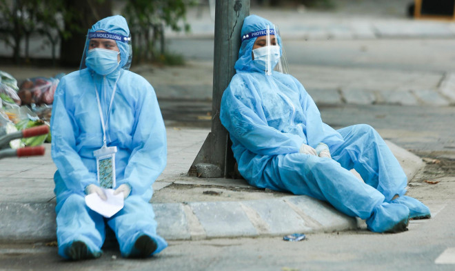 Các nhân y tế trong bộ đồ bảo hộ, ngồi dưới gốc cây sau một ngày làm việc căng thẳng tại ổ dịch phường Thanh Xuân Trung
