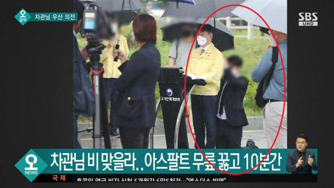 Trợ lý quỳ gối che ô cho Thứ trưởng Tư pháp Hàn Quốc.