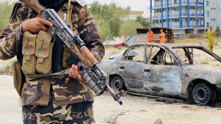 Một tay súng Taliban đứng canh gác cạnh xác một chiếc ô tô được IS dùng làm bệ đỡ để phóng rocket vào sân bay quốc tế Kabul. Ảnh: EPA-EFE