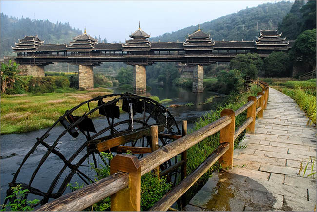 Đứng trên cầu, bạn có thể nhìn thấy bánh xe nước lớn quay chậm, những ngôi nhà của tộc Đồng nằm dọc bên sông và gần núi.
