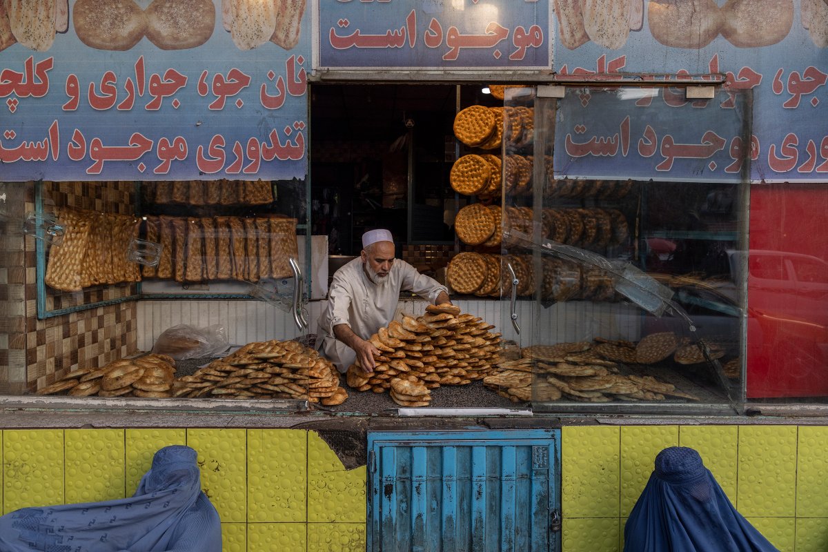 Hai phụ nữ Afghanistan ngồi xin ăn trước cửa hàng bán bánh ở Kabul hôm 13/9. Ảnh: New York Times