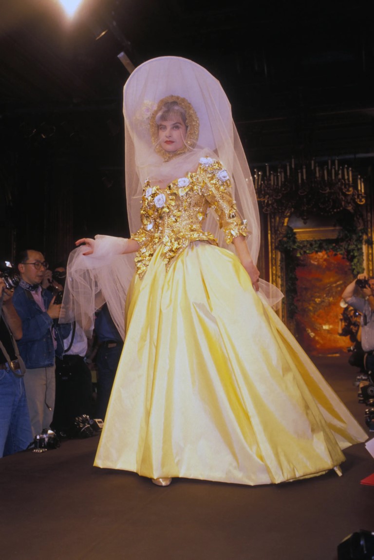 Người mẫu mặc váy cưới màu vàng những năm 1980 với thêu hoa và đội mũ trắng hình tròn với mạng che mặt trắng.&nbsp;Christian Lacroix Thu / Đông 1988