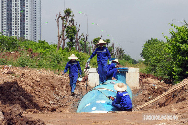 Công nhân cùng thiết bị máy móc đang thi công lắp đặt đường ống tại khu vực đường gom Đại lộ Thăng Long.