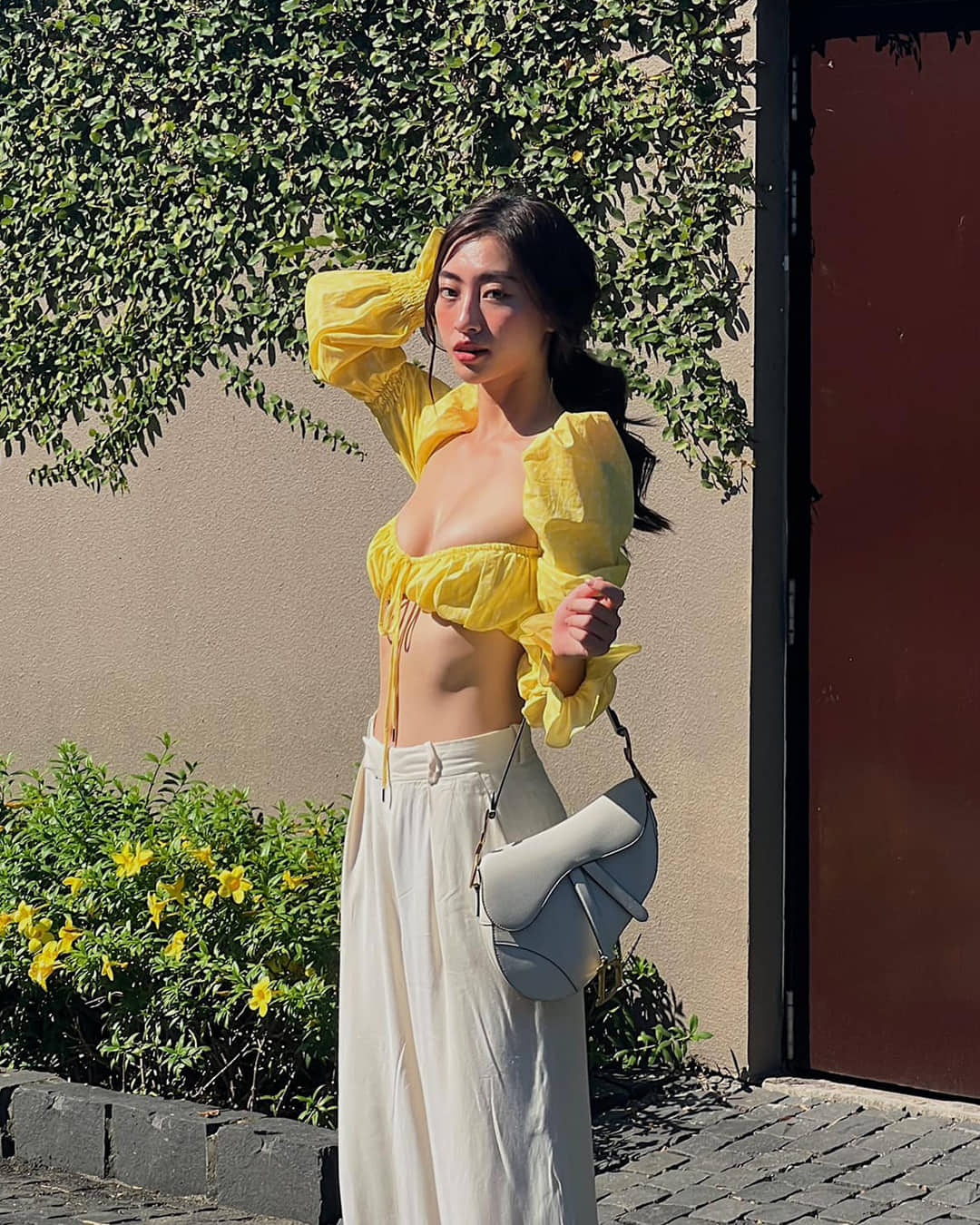 Hoa hậu Lương Thùy Linh diện áo croptop có dáng cổ vuông màu vàng nổi bật. Cô kết hợp item này với chiếc quần vải màu trắng cạp cao.