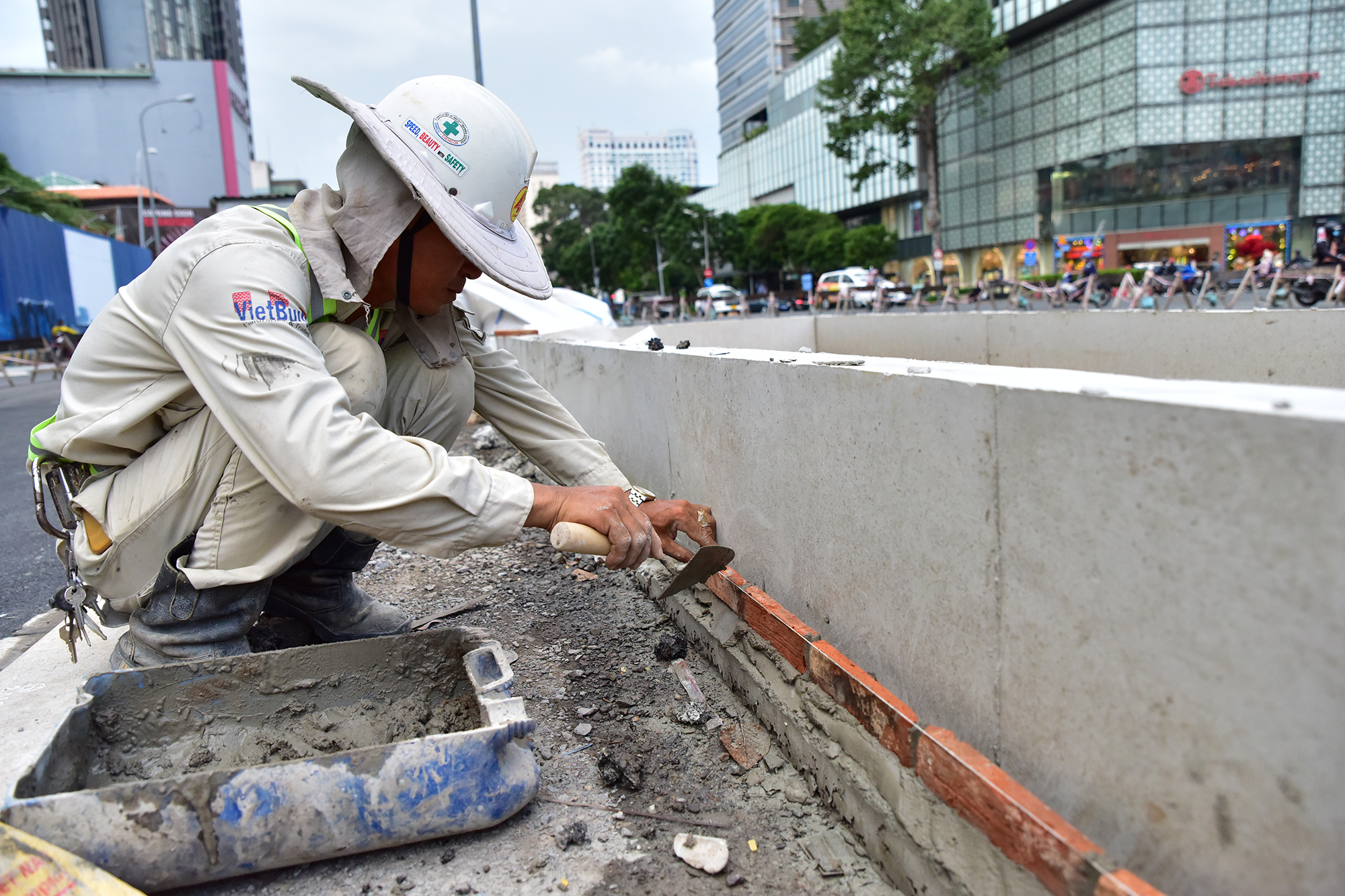 Công nhân lắp các viên gạch trang trí bồn cây tại đoạn vừa được hoàn thành trải nhựa. Một công nhân cho biết việc thi công, trang trí phải hoàn thành trước 2/9.