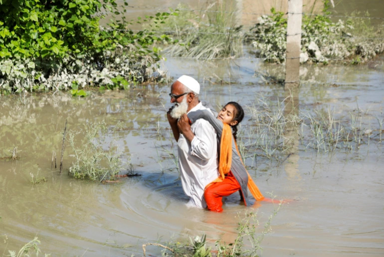 Người đàn ông cõng bé gái lội trong nước lũ ở Pakistan (ảnh: Aljazeera)