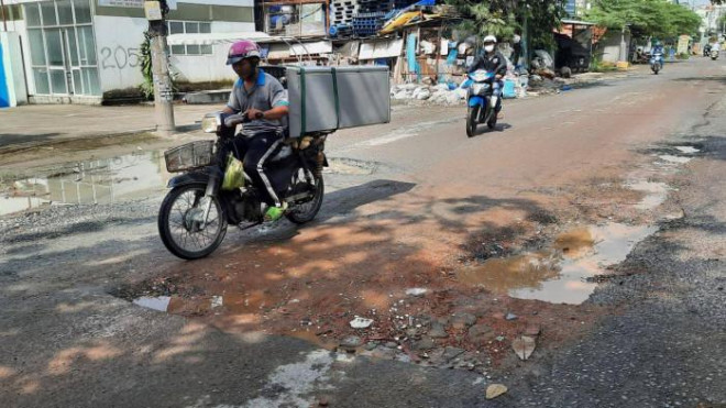 Dù từng được trải nhựa cách đây 2 năm nhưng hiện nay tuyến đường Bưng Ông Thoàn đang xuống cấp nghiêm trọng. (Trong ảnh, người dân đã dùng xà bần để trám các ổ gà nhưng trám rồi đường vẫn như cũ). Ảnh: Quang Phương.