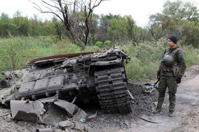 Binh sĩ Ukraine đứng kế một xe tăng Nga bị phá hủy ở tỉnh Kharkiv. Ảnh: REUTERS