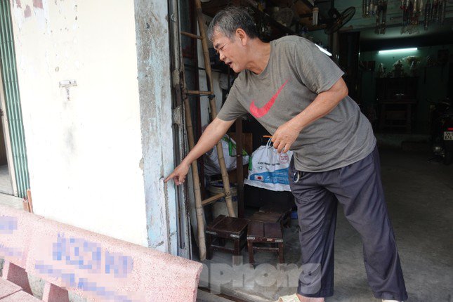 "Đến nay mực nước ngày càng cao, nền thì không thể tiếp tục nâng lên được nữa vì trần nhà đang thấp lắm rồi ! Do đó tôi phải tự thiết kế một tấm bảng thép có sẵn khe rãnh để lắp đặt trước cửa nhằm ngăn nước và rác thải tràn vào nhà khi có mưa lớn"- ông Long chia sẻ. (Ảnh: ông Long chỉ cho Phóng viên xem nơi đặt công cụ ngăn nước, chống ngập cho căn nhà)