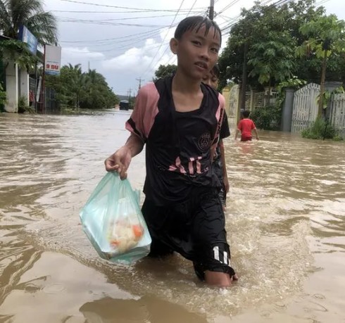 Trẻ em cầm hộp cơm trên đường trong biển nước.