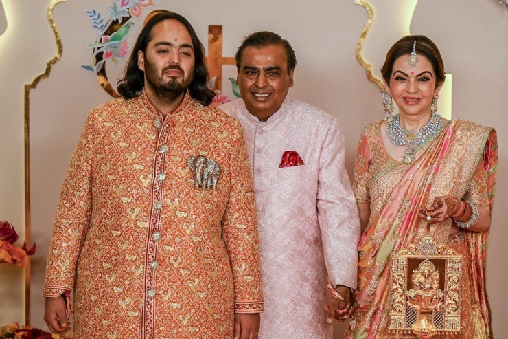 Chú rể Anant Ambani (bìa trái) xuất hiện cùng bố mẹ. Bà Nita Ambani trong bộ trang phục sherwani, hoa văn cầu kỳ. Bộ trang phục sherwani của chủ rể được thêu bằng chỉ vàng, cân bằng giữa phong cách truyền thống và đương đại. Anh kết hợp với quần màu ngà, tôn thêm sự sang trọng bằng chiếc trâm cài đính đá quý.