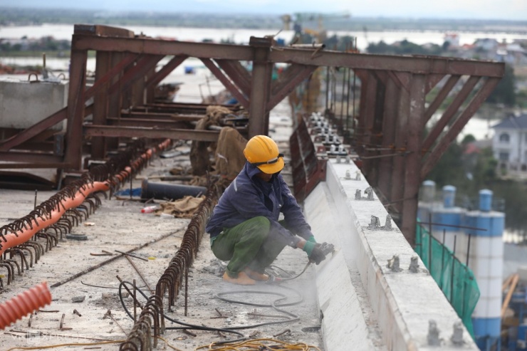 Công nhân dùng máy mài đánh bóng lan can cầu. Miền Trung đang nắng nóng, nhiệt độ ngoài trời trên 35 độ C.