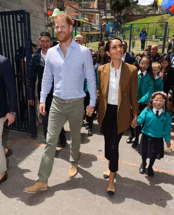 Sang ngày thứ hai, Meghan mặc blazer Loro Piana Jamilla màu camel có giá 3.750 USD, áo sơ mi Mango trắng 45 USD, giày đế bệt hở gót của Chanel trị giá 1.100 USD và đeo túi Cesta 765 USD.