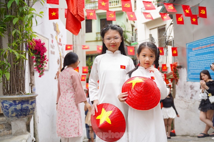 Hai em bé mặc áo dài cầm trên tay nón lá hình Quốc kỳ chụp hình tại ngõ cờ hoa Yên Phụ.