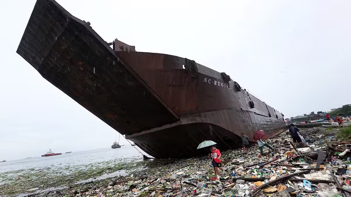 Người dân ở thành phố Navotas đi qua một sà lan bị mắc cạn ở bờ biển với nhiều mảnh vỡ, rác bị cuốn bên dưới.