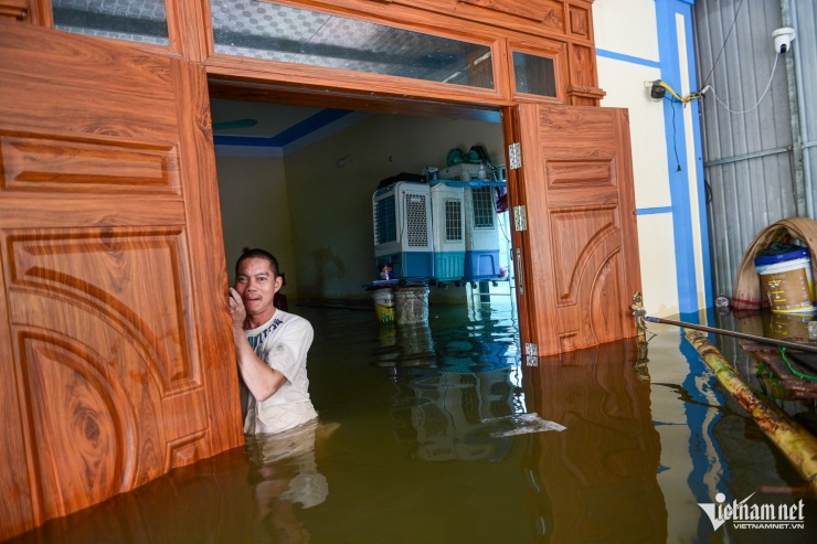 9h hôm nay, mưa ngưng, anh Nguyễn Văn Kết (48 tuổi) dùng bè chuối tự chế vào nhà gia cố, kiểm tra đồ đạc. Đây là lần thứ 3 anh phải nâng độ cao giá đỡ đồ lên theo mực nước tăng.