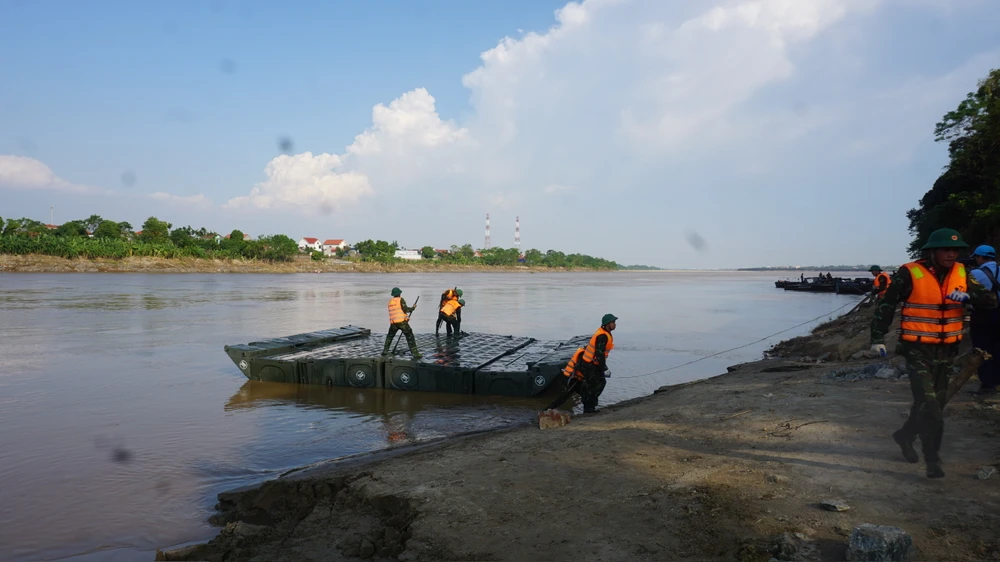 Trong ảnh là hai chiếc xe chuyên dụng, mỗi xe chở một đốt phao lùi xuống dốc đầu Tam Nông. Đến vị trí mép nước, đốt phao được thả xuống, mở bung ra. Tiếp đó, chiến sĩ công binh phải thao tác để khóa cứng các khớp xoay. Ảnh: XUÂN NGUYỄN