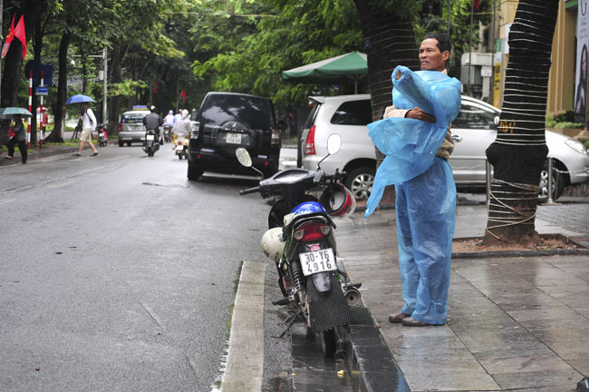 Nhiều người đi đường phải dừng lại mặc áo mưa vì những cơn mưa bất chợt, lúc to, lúc nhỏ.