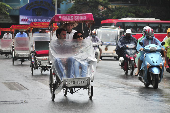 Hai du khách nước ngoài đi xích lô phải quàng thêm áo mưa để tham quan Hồ Gươm.