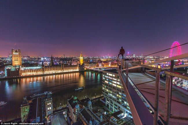 Tòa nhà quốc hội Anh in bóng xuống dòng sông Thames ở London, với vòng quay London Eye sáng hồng trong đêm.