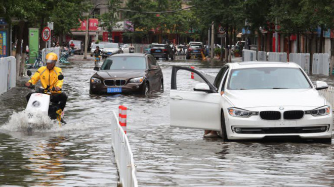 Tài xế Meituan đi xe điện vào khu vực đường phố ngập lụt. Tờ People's Daily viết họ phải "mạo hiểm cuộc sống vì miếng ăn". Ảnh: Getty Images.