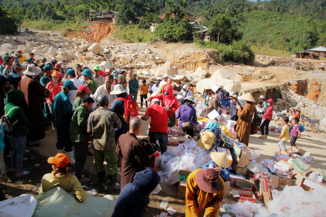 Người dân xã Phước Thành nhận hàng cứu trợ bên cạnh đống đổ nát vì lũ cuốn