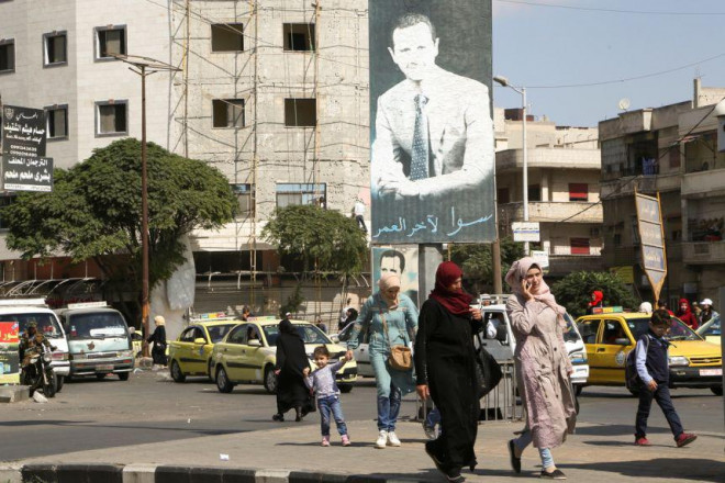 Người dân đi ngang tấm áp phích có hình Tổng thống Syria Bashar al-Assad ở TP Homs, Syria, vào ngày 3-10. Ảnh: Reuters
