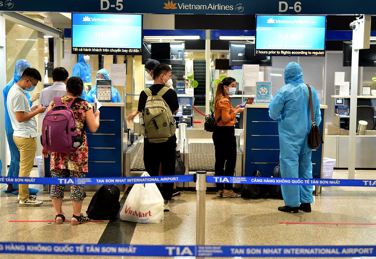 Hành khách đi chuyến bay của Vietnam Airlines đi Hà Nội xếp hàng chờ làm thủ tục. Hãng bay này bố trí khá nhiều nhân viên, trang bị đầy đủ đồ bảo hộ để hỗ trợ, hướng dẫn khách các làm thủ tục.