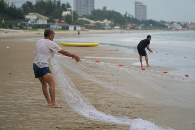 Một người đàn ông vừa tranh thủ tắm biển, vừa kéo lưới đánh cá