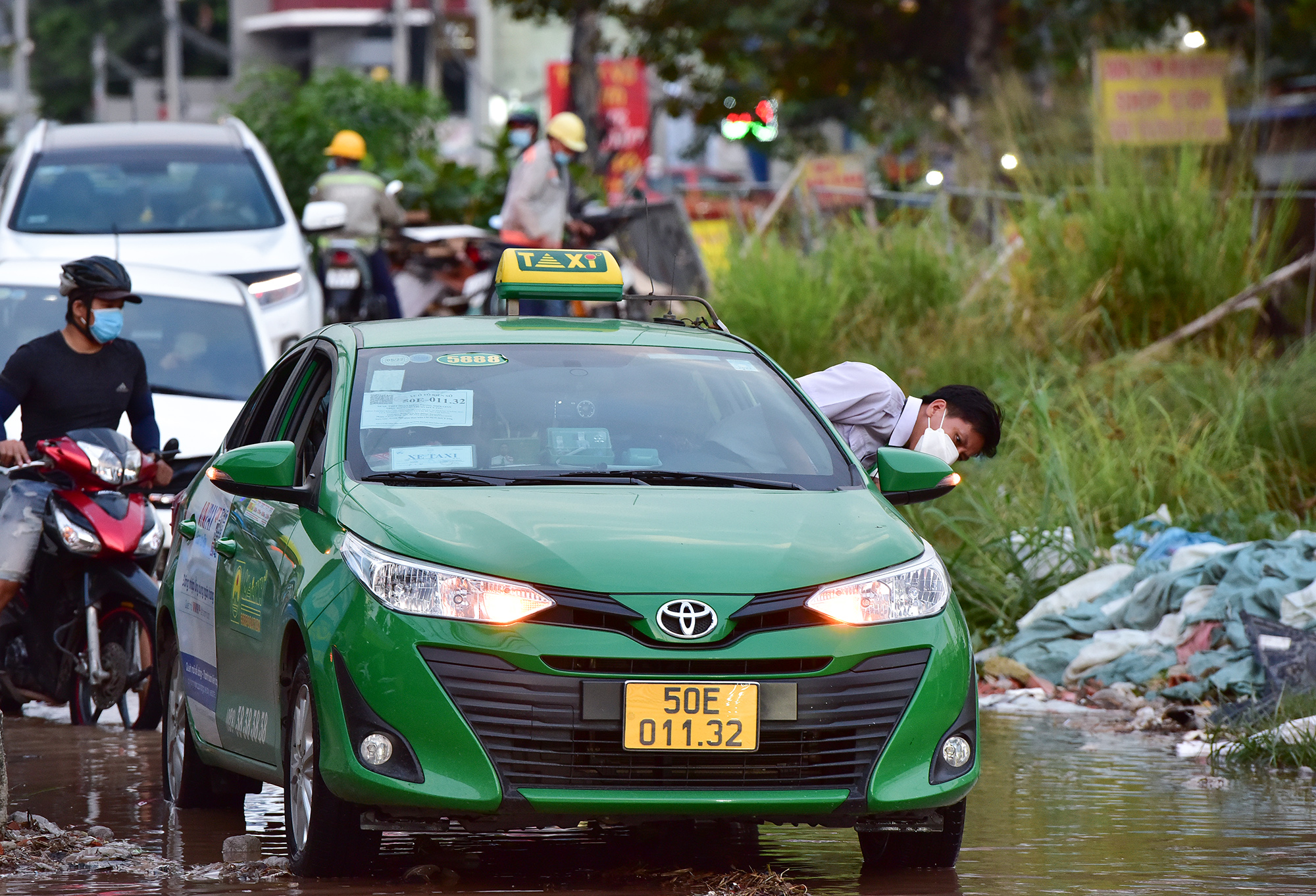 Tài xế taxi phải dừng lại giữa đường để kiểm tra gầm xe do đụng phải đá lớn khi né phần đường ngập nước.