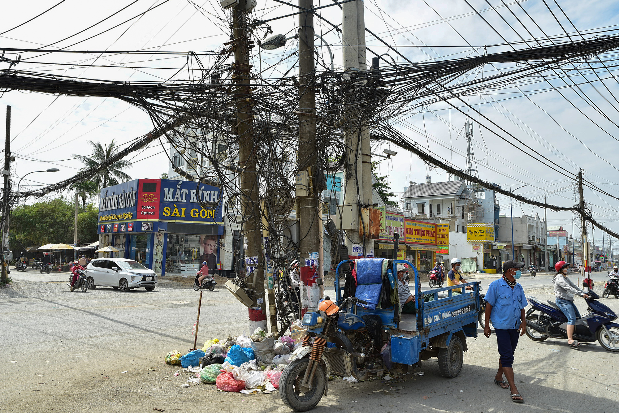 Bốn trụ điện với dây, ổ cáp viễn thông tạo thành "mạng nhện" nằm ngay giữa ngã tư đường. "Bà con rất mừng khi tuyến đường được mở rộng lên gấp 4 lần nhưng tình trạng hàng trăm trụ điện cứ sừng sửng&nbsp;giữa đường kéo dài thế không chỉ gây mất an toàn cho người đi đường mà mỹ quan đô thị trở nên xấu xí", ông Lê Văn Phong, ngụ&nbsp;xã Thới Tam Thôn, phản ánh.